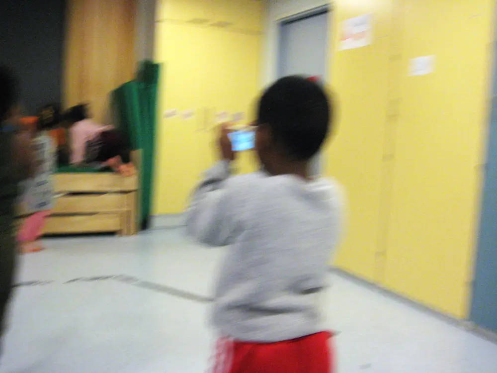 A photograph showing a child moving around and taking photos of dancing children with a camera in the daycare centre&rsquo;s multipurpose room.