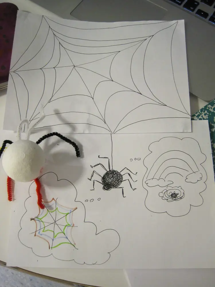 The photo shows a spider made from a paper ball, placed on top of a drawing. The drawing shows a black spiderweb and a spider with two thought bubbles coming from it: one thought bubble contains a colourful spiderweb, and the other shows the spider in its web under a rainbow.