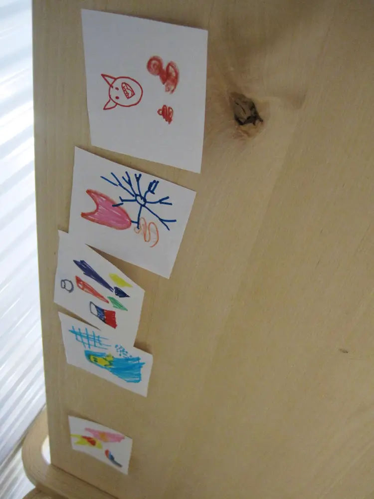 The image shows what the children see attached to the underside of the bench: five colourful drawings featuring, among other things, an animal figure, hearts, human figures, a snowflake, and other colourful shapes.