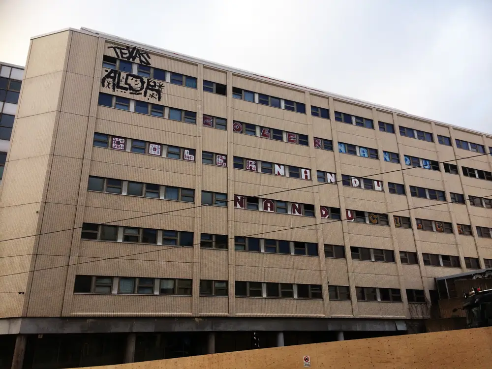 A photograph of an abandoned office building with six stories of windows visible on its facade. Some of the windows and walls are covered in graffiti.