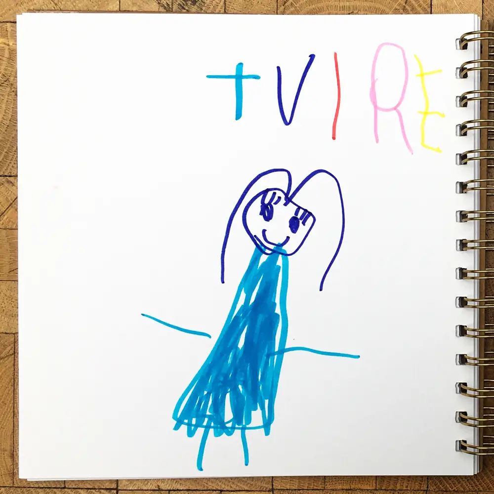 A child's drawing in a square spiral-bound notebook, featuring a light-blue character with the word "TUIRE" written above it in different-coloured letters. The character has long purple hair and looks happy.