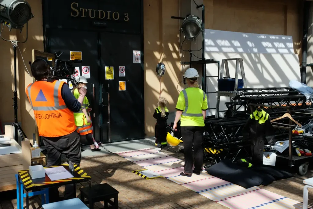 A photograph taken outside the studio, with preparations for the event underway. The photo shows the researcher, a child holding a helium balloon, an adult standing and watching the child, and a person filming the event.