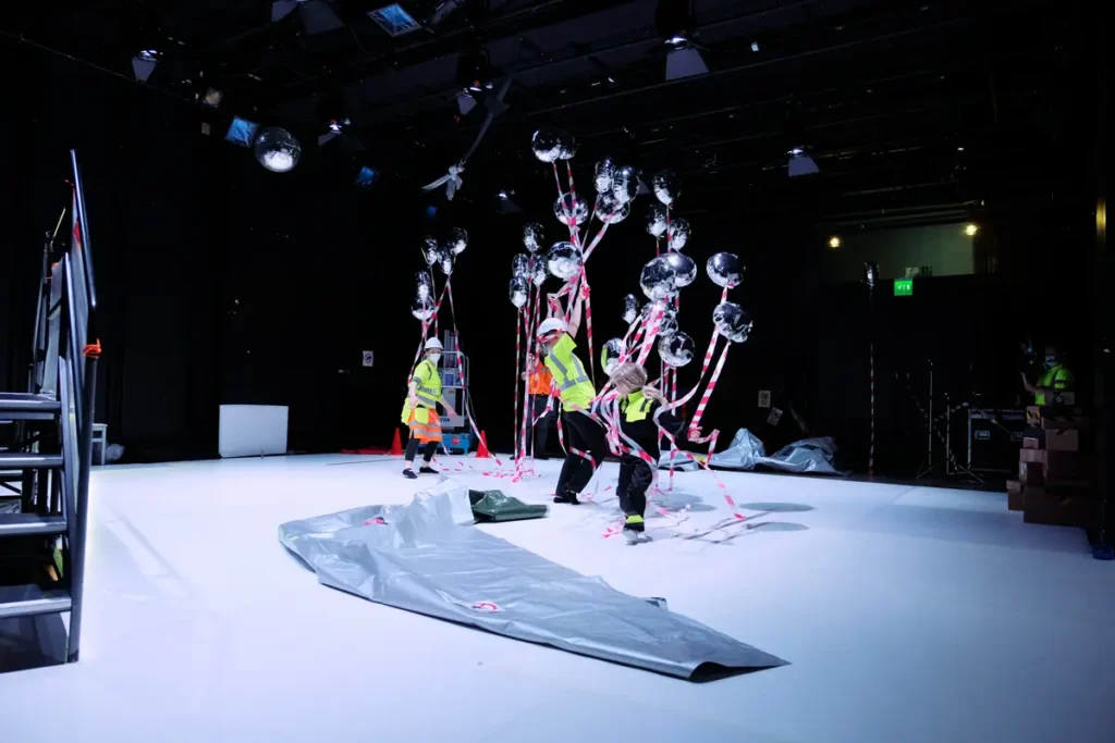 The collage features six photographs showing a researcher, a participating child, and an adult in construction gear lifting a large grey tarp, revealing a profusion of silver helium balloons with red-and-white ribbons dangling from them. The photos capture the moment the balloons are released and begin to rise.